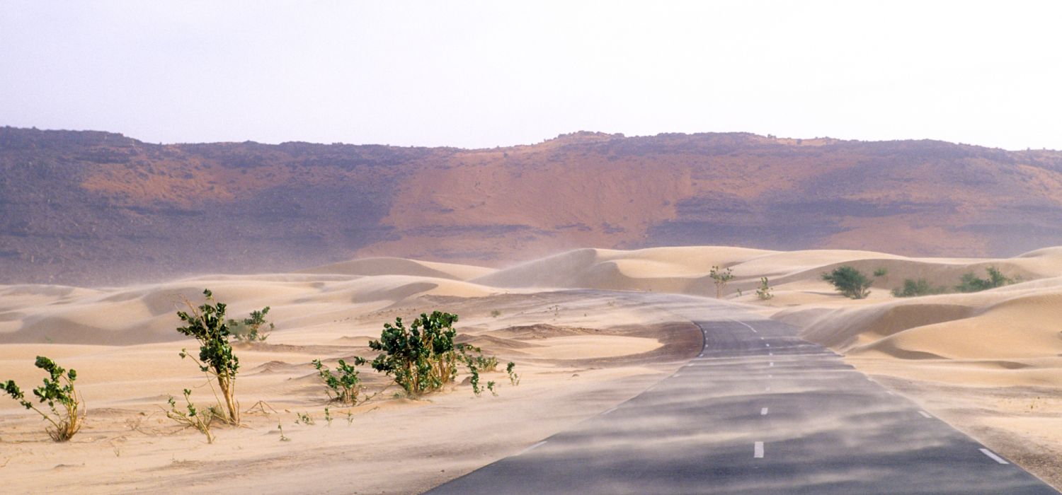 New paved road near the capital in the middle of the desert with wind and sand. Crag in the background. In Mauritania