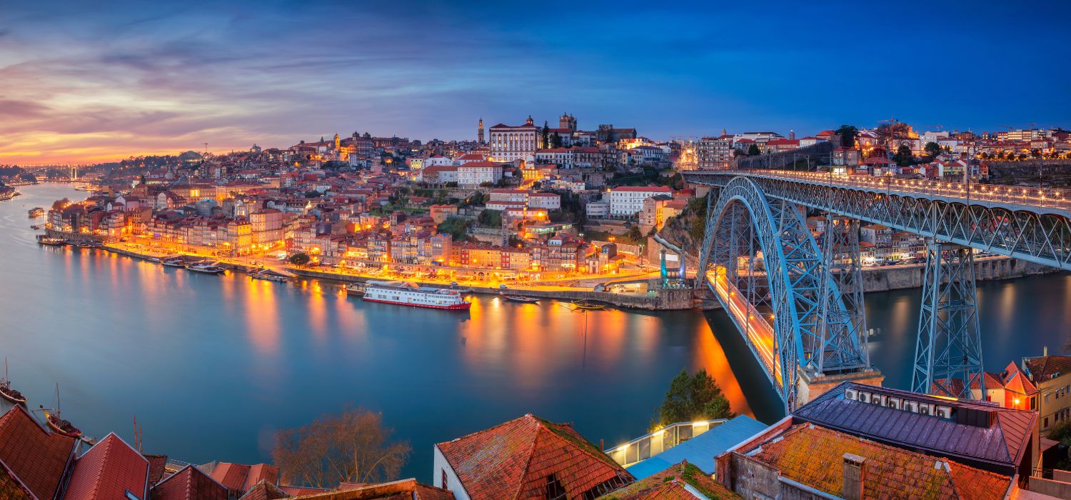 Panoramic cityscape image of Porto, Portugal with the famous Luis I Bridge and the Douro River during dramatic sunset.