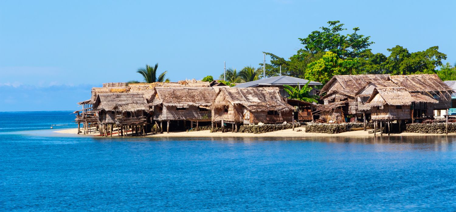 Photo of traditional thatched houses on a beautiful beach in Auki, the provincial capital of Malaita Province, Solomon Islands